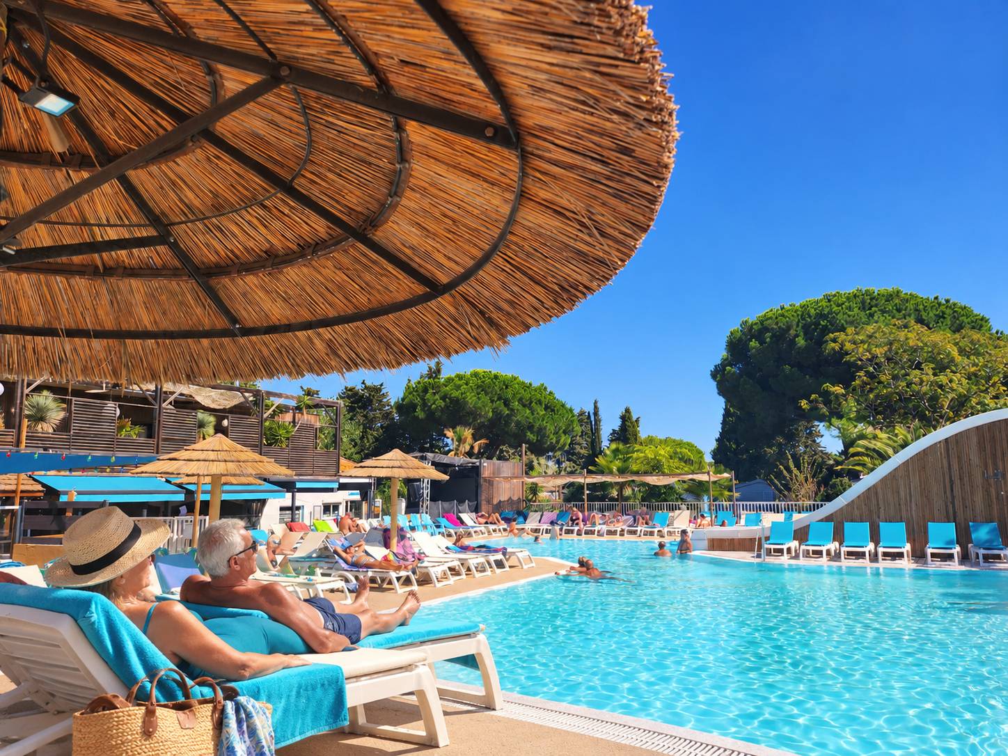 Couple de retraités se détendant au bord de la piscine chauffée du camping Les Sablettes, séjour longue durée au Grau d'Agde